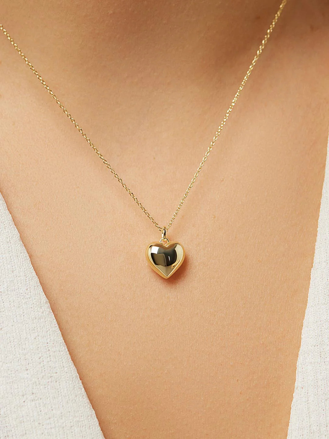 Gold heart-shaped necklace on a person wearing a white top