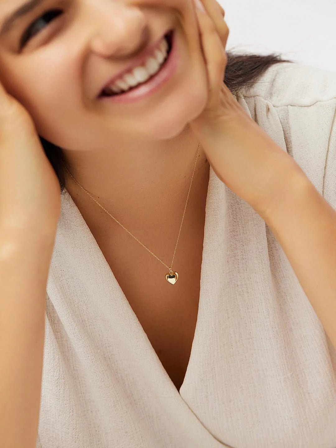Woman wearing unjellic gold necklace with a heart pendant, smiling.
